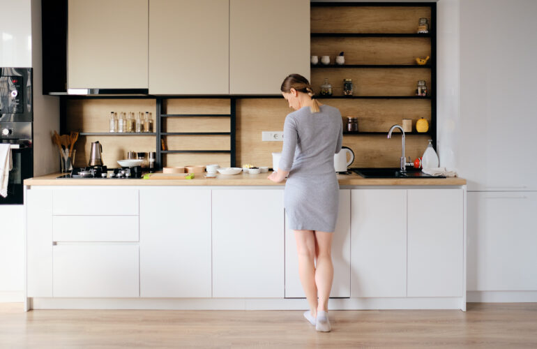 Young woman with beautiful body standing next to a modern kitchen while cooking. Back view